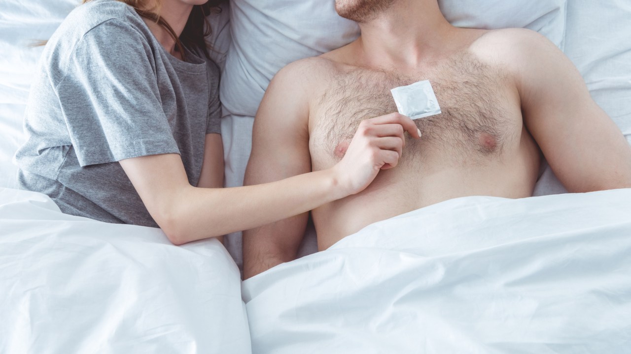 Casal na cama segurando camisinha