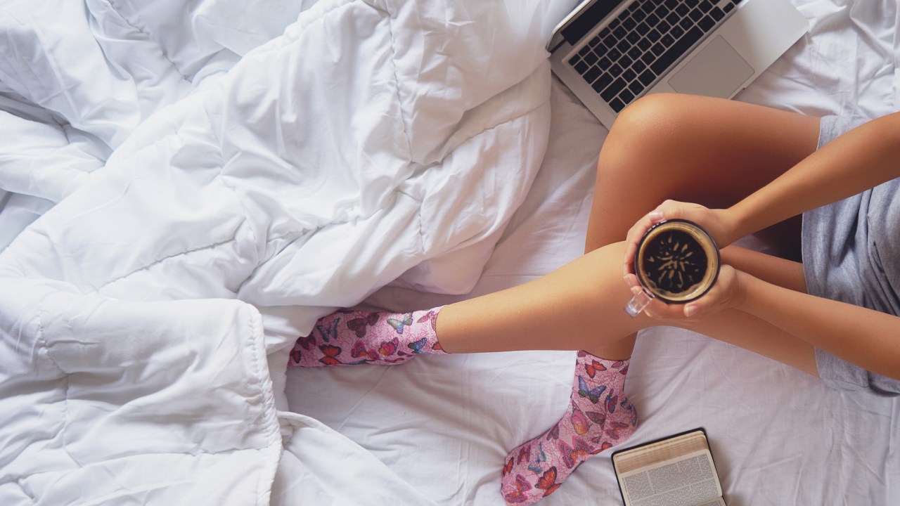 Mulher na cama com computador, caderno e café