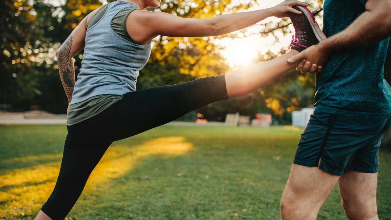 Mulher alongando ao ar livre com a ajuda de um personal trainer