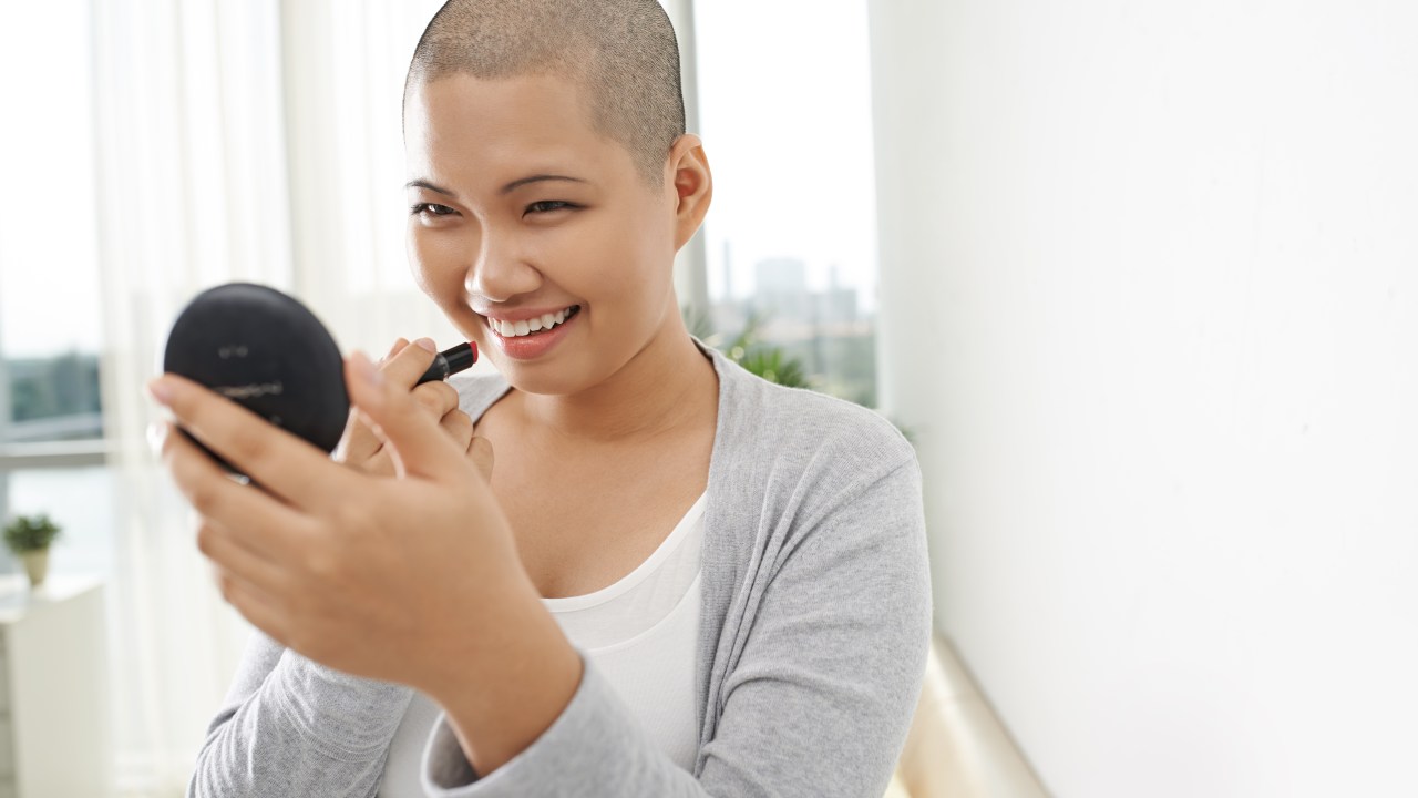 Mulher careca com cancer de mama passando maquiagem