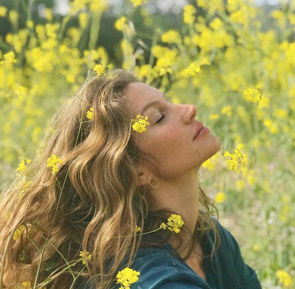 Mulher sentada no jardim de olhos fechados, sentindo o sol na pele e flores nos cabelos