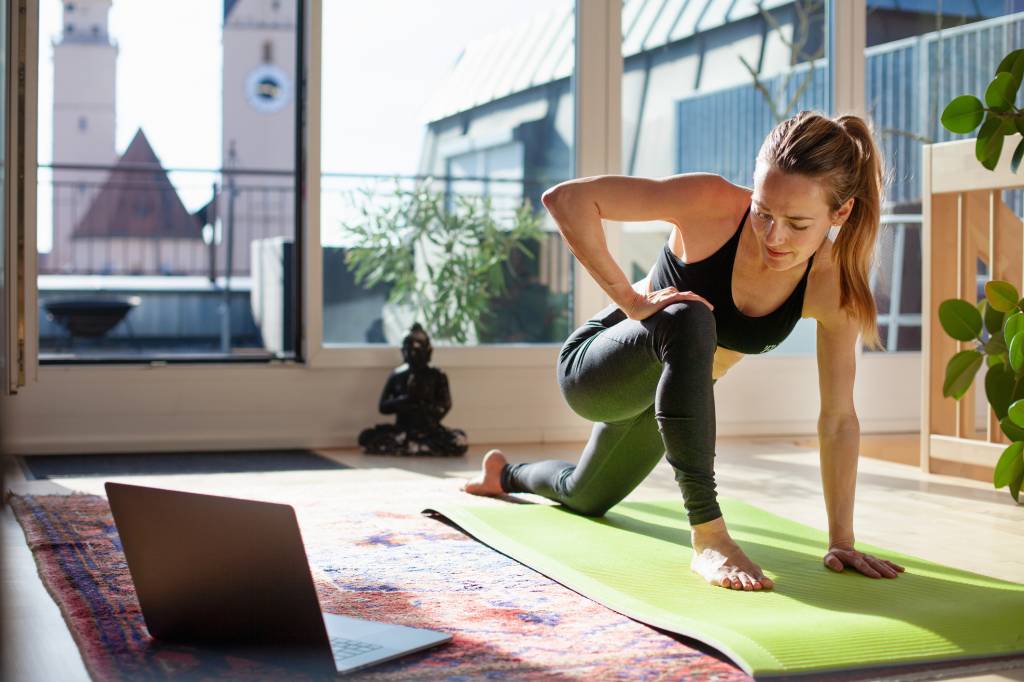 Woman exercising at home in front of her laptop, stretching her legs Woman exercising at home in front of her laptop, stretching her legs