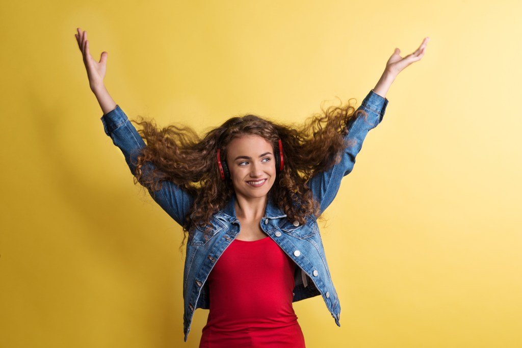 Portrait of a young woman with headphones in a studio on a yellow background. mulher mexendo nos seus cabelos