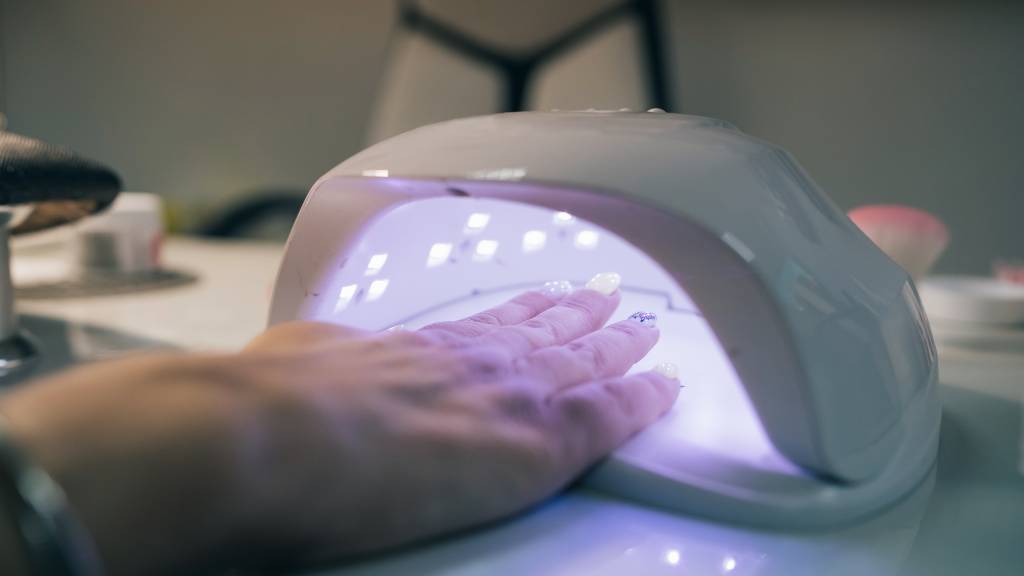 UV lamp gel polish manicure process. Salon procedure. The master coats the client’s nails with a varnish.