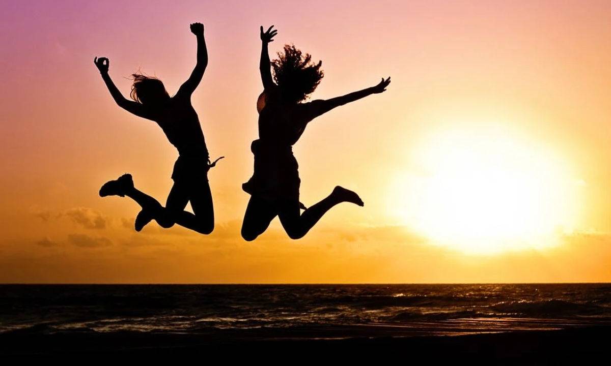 Silhueta de duas pessoas saltando com sol ao fundo