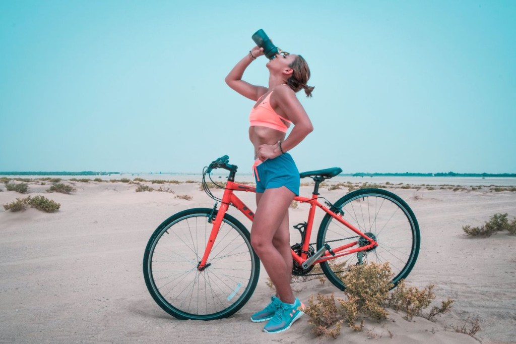 exercício-calor (1) Mulher bebendo água com bicicleta ao lado