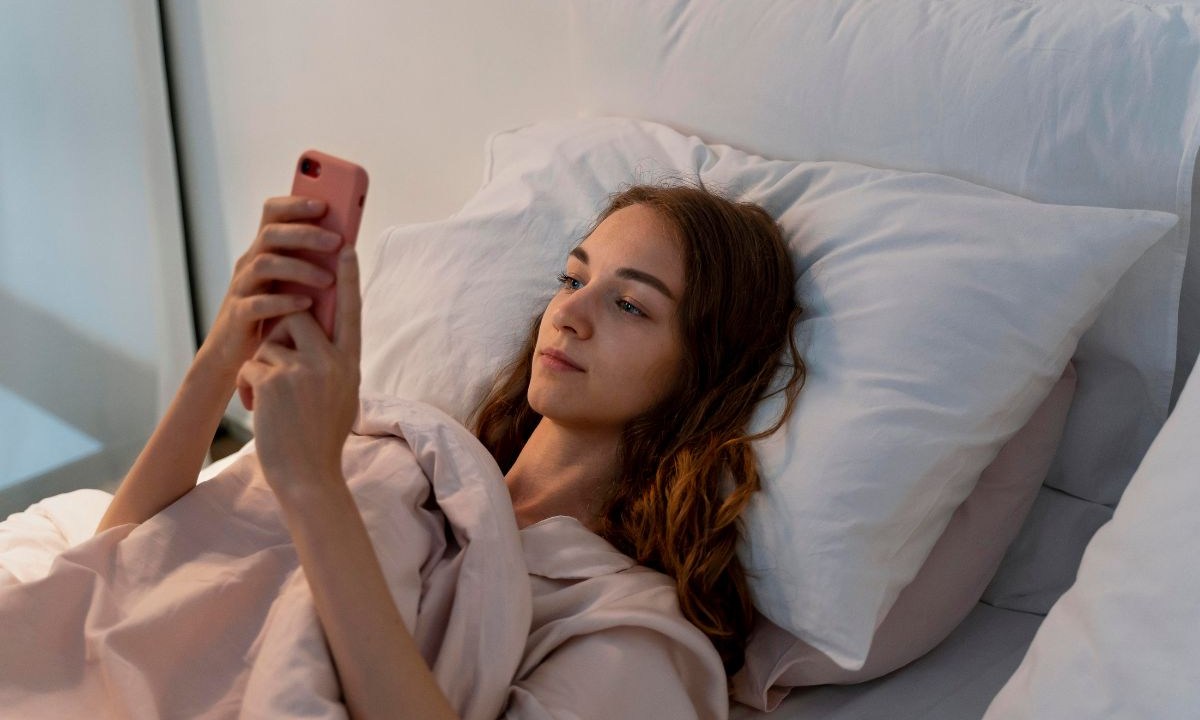 Mulher utilizando celular deitada na cama