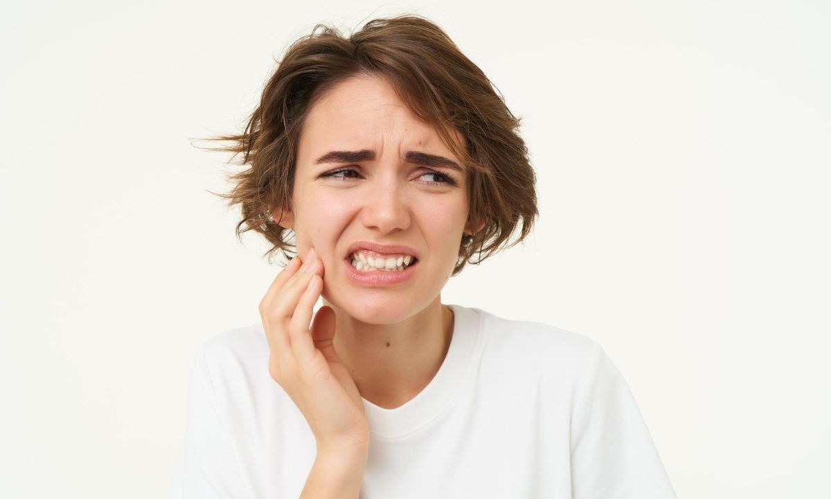Mulher vestindo camiseta branca e sentindo dor de dente