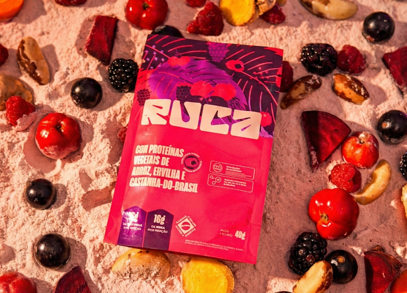 Embalagem rosa da marca Ruca com proteínas vegetais de arroz, ervilha e castanha-do-brasil, cercada por frutas vermelhas, castanhas e vegetais picados sobre uma superfície clara